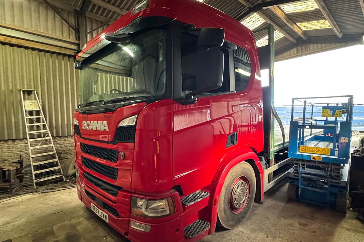 Red Scania truck undergoing full vehicle wrap installation in workshop